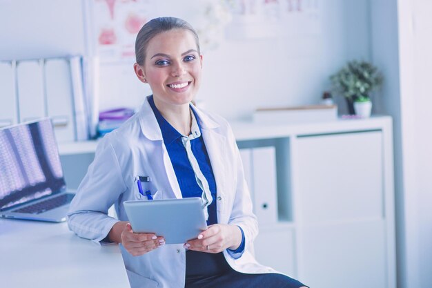 Portrait of woman doctor at hospital corridor holding tablet computer looking at camera smiling