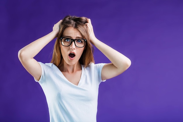 Portrait of woman dressed in white tshirt and eyeglasses make shock grimace on face isolated on blue studio background