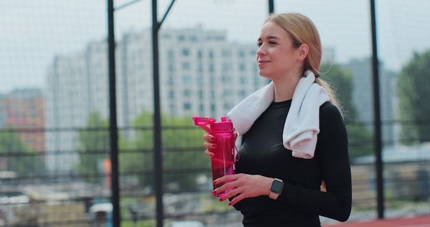 Portrait of a woman drinking water from the pink sport bottle Fit girl drink water from bottle Rest after hard basketball train Sport activities