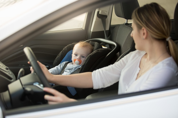Portrait of woman driving car with baby sitting on front seat