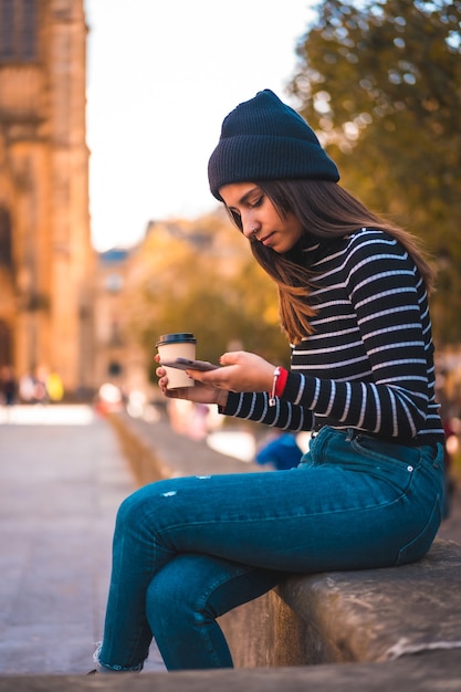 モバイルを使用しながら公園でコーヒーを楽しむ肖像画の女性