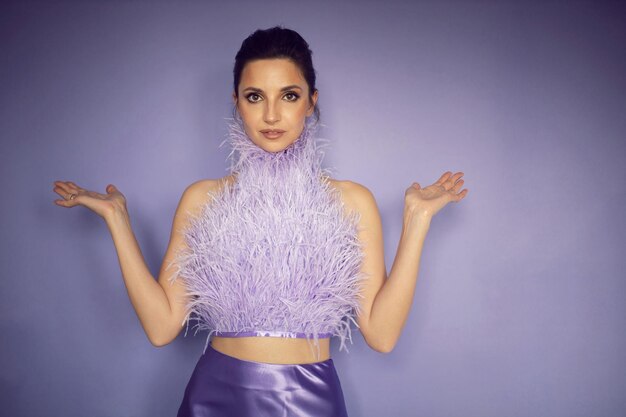 Portrait woman in an evening purple dress with feathers stands in the background in the studio