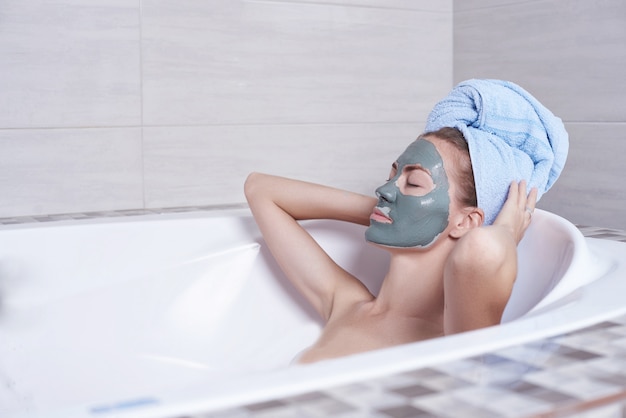 浴室のレトロなお風呂で横になっている顔のアルギン酸マスクの女性の肖像画