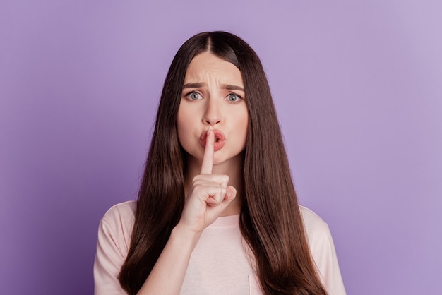 Portrait of woman finger close lips isolated on purple background