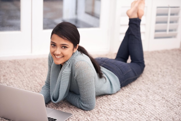 パソコンと一緒に床に横たわっている女性の肖像画 笑顔とリラックス 勉強 大学研究とウェブブラウジング 大学生女の子 カーペットでコンピュータの電子学習とオンライン教育を家庭で