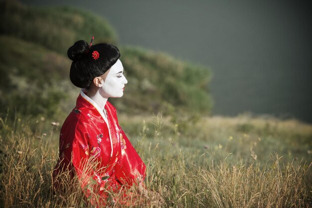 Portrait of a woman in geisha makeup sitting by the riverside