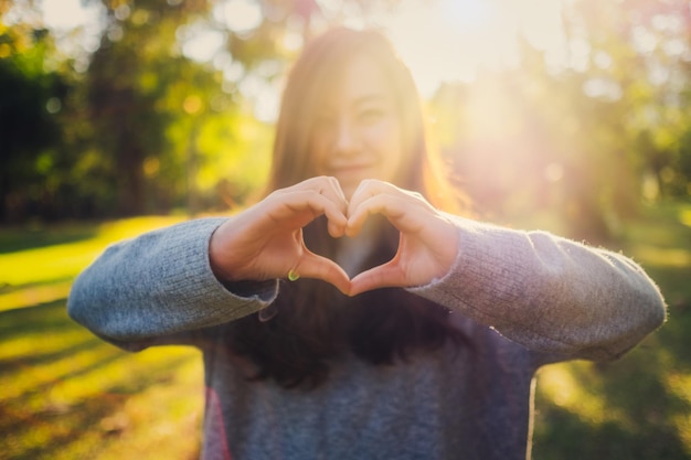 Photo portrait of woman gesturing heart shape while standing at park