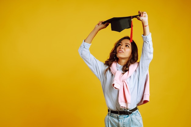 Portrait of woman in a graduation hat on her head posing on yellow.