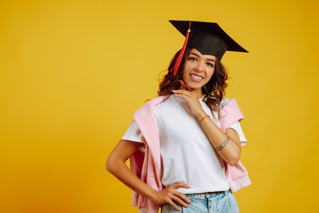 Ritratto di donna in un cappello di laurea sulla sua testa in posa sul giallo.