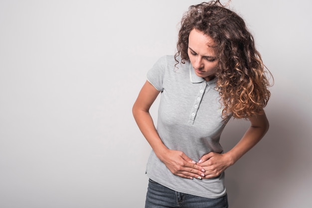 Portrait of woman having stomachache against gray background