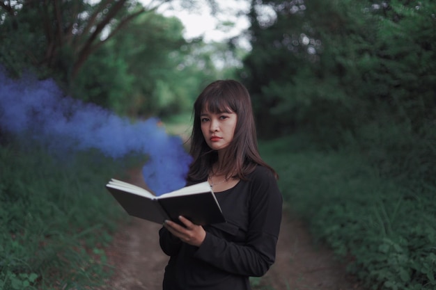 portrait of woman holding book while standing in forest