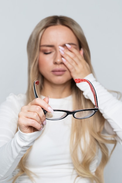 Portrait of woman holding her glasses while rubbing her eyes