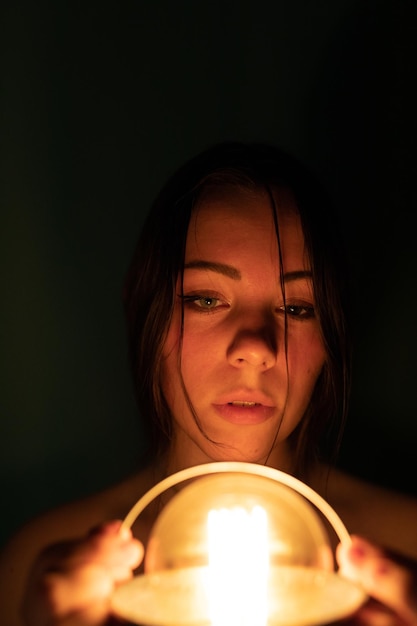 Foto ritratto di una donna che tiene una lampadina illuminata in camera oscura