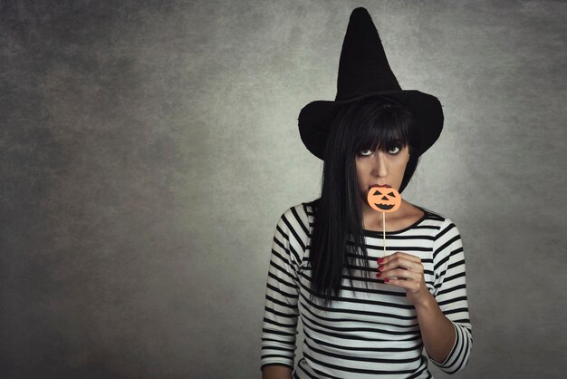 Portrait of woman holding jack o lantern candy while standing against gray wall