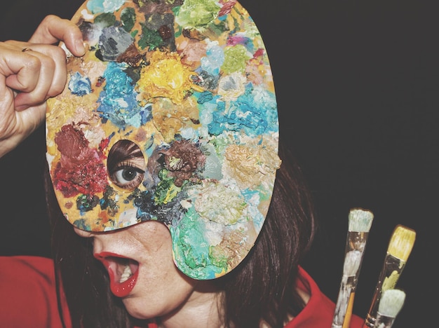 Photo portrait of woman holding multi colored palette by face against black background