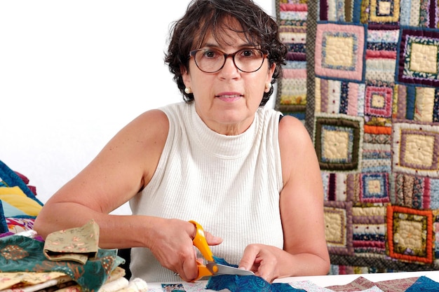 Photo portrait of woman holding scissor while doing patchwork on table at home