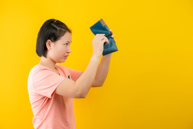 Portrait of a woman holding a wallet regretting that there is no money in her purse against a yellow background.concept saving.