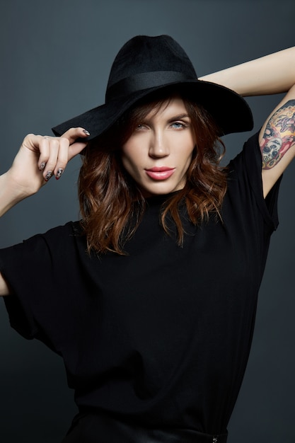 Portrait of a woman in a large black hat on a dark wall