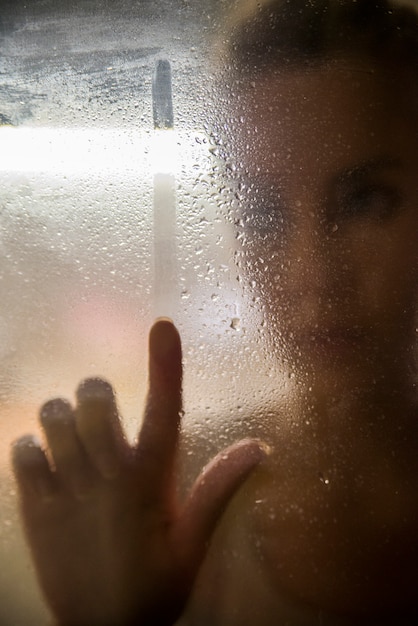 雨の日に窓から見える女性の肖像画。窓から見える女性。女の子が雨の後に窓を見ている。ポートレート