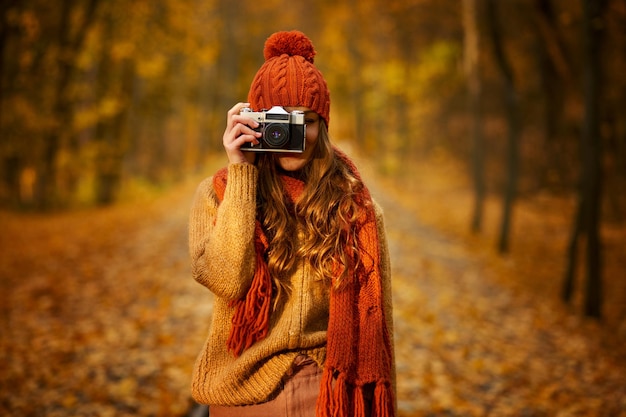 レトロなカメラを保持している女性写真家の肖像画。秋の公園の女の子。背景がぼやけている