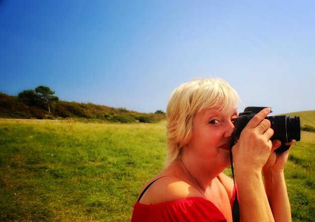 Portrait of woman photographing against sky