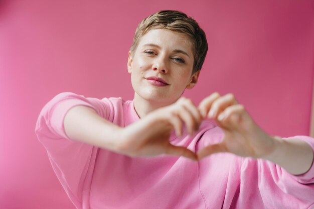 Portrait of woman in pink shaping heart with her hands