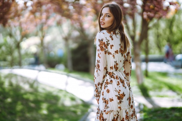 Portrait of  woman in a pretty dress with flowers enjoys blooming green garden in spring day. Fashion and style concept.