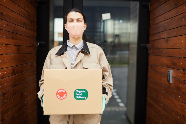 Portrait of woman in protective mask working as a courier she standing outdoors and holding cardboard box