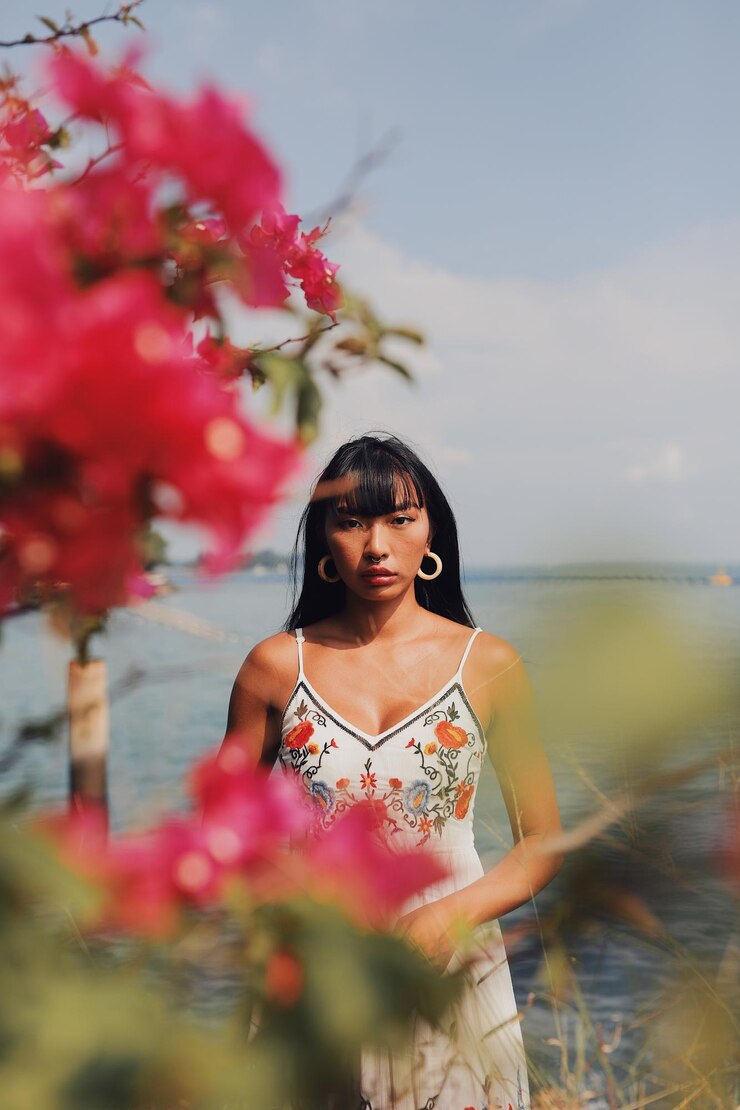 Photo portrait of woman seen through flowering plant standing at beach against sky