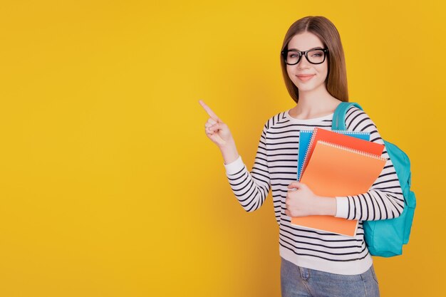 Portrait of woman showing finger direct empty space hold copybook on yellow wall