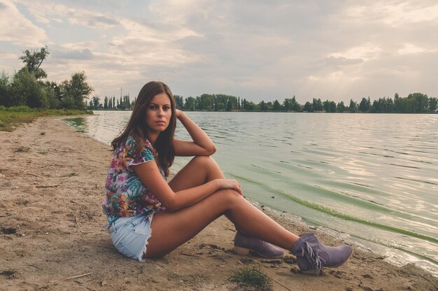 Foto ritratto di una donna seduta sul lago contro il cielo