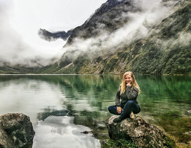 Photo portrait of woman sitting by lake on rock