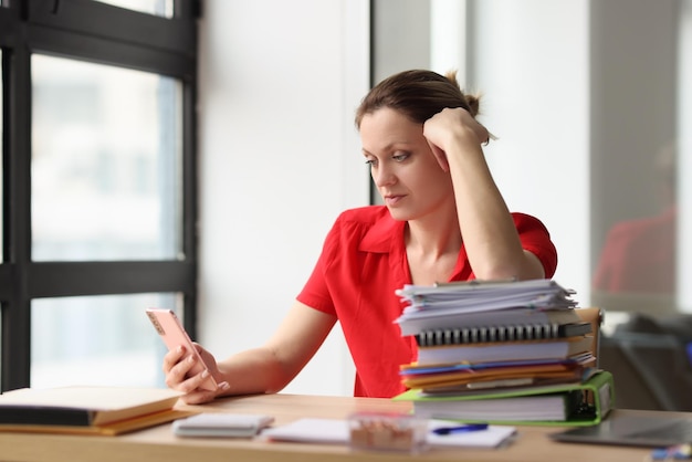 Portrait of woman sitting at desk littered with papers female surfing internet using modern