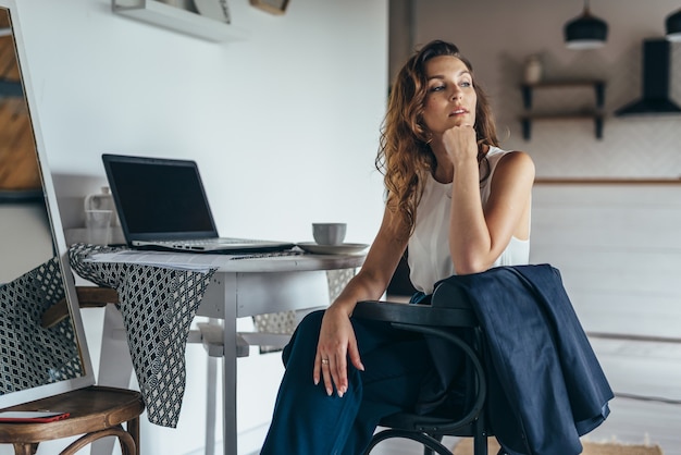 Portrait of a woman sitting in the kitchen with a laptop at the table. Work from home.