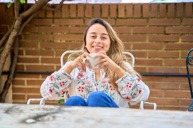 Photo portrait of a woman sitting outside with a cup of coffee in her hand looking at the camera