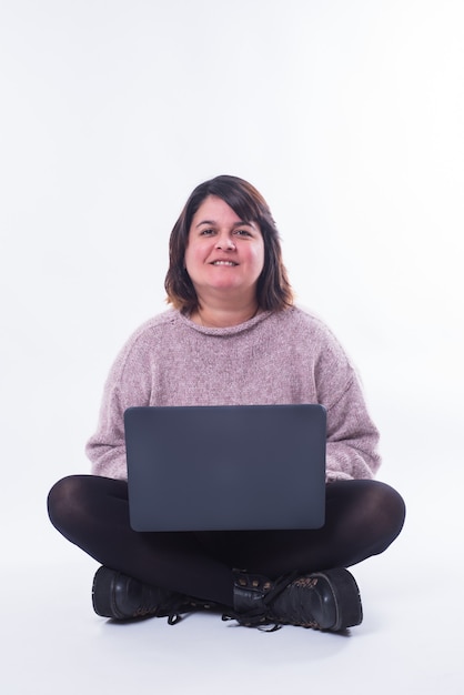 Portrait of a woman sitting with her personal computer looking at camera in white background. Internet shopping concept. Copy space