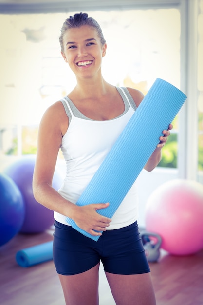 Ritratto di donna sorridente mentre si tiene la stuoia di yoga