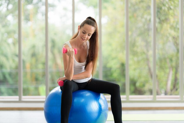 Portrait of woman in sportswear exercising with dumbbells indoors at home or gym