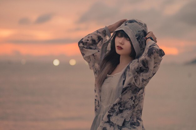 Portrait of woman standing at beach against sky during sunset