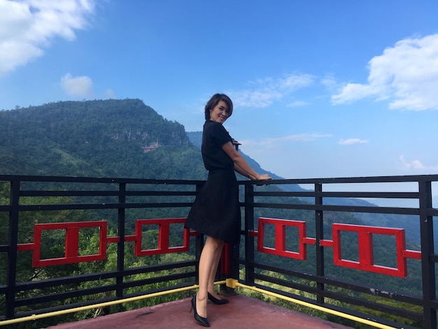 Portrait of woman standing by railing against sky