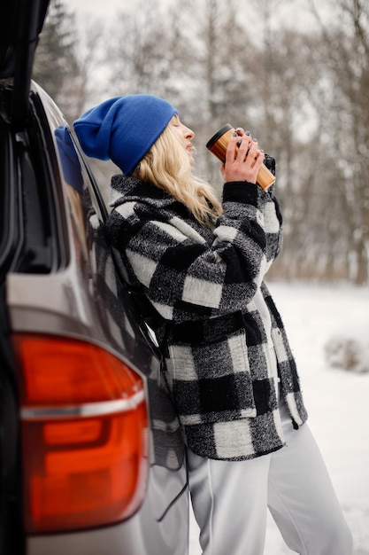 Ritratto di una donna in piedi vicino al bagagliaio di un'auto aperta nella foresta invernale