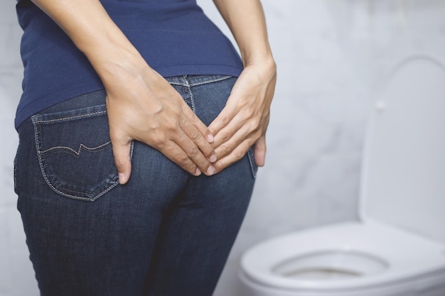 Photo portrait of a woman suffers from diarrhea his stomach painful ache and problem hand hold tissue paper roll in front of toilet bowl constipation in bathroom hygiene health care concept