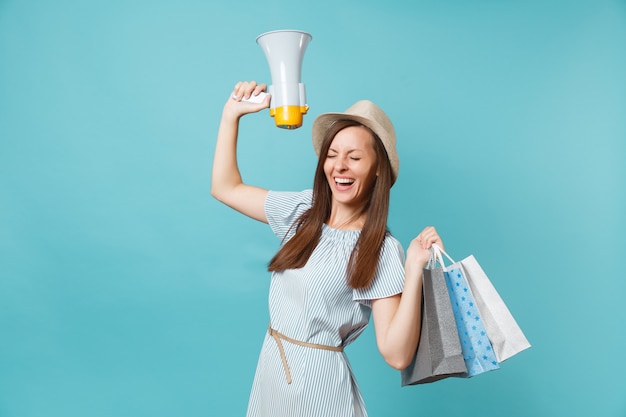 Portrait woman in summer dress, hat holding packages bags with purchases after shopping, scream in megaphone, announces discounts sale isolated on blue pastel background. Copy space for advertisement.