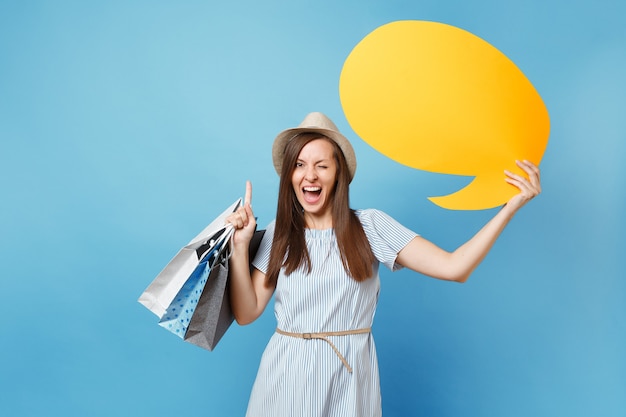 Portrait of woman in summer dress, straw hat holding packages bags with purchases after shopping, empty blank Say cloud, speech bubble card isolated on blue pastel background. Copy space advertisement