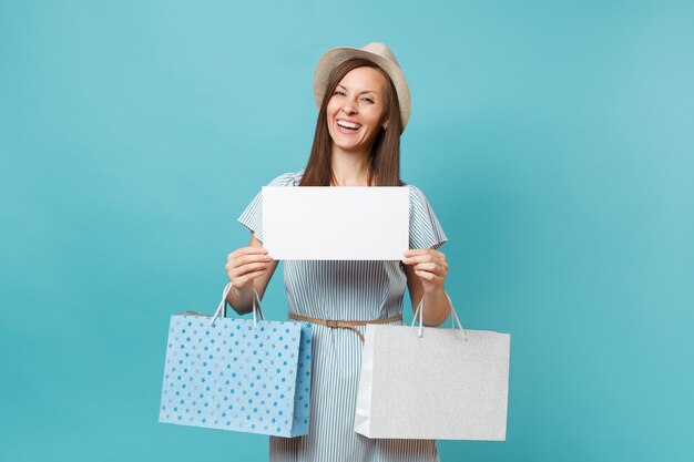 Portrait of woman in summer dress, straw hat holding packages bags with purchases after shopping, empty blank Say cloud, speech bubble card isolated on blue pastel background. Copy space advertisement