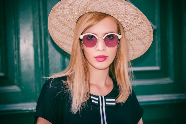 portrait of woman in sunglasses and hat standing against door