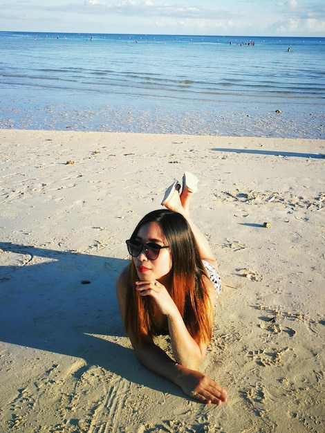 Foto ritratto di una donna con gli occhiali da sole sdraiata sulla spiaggia