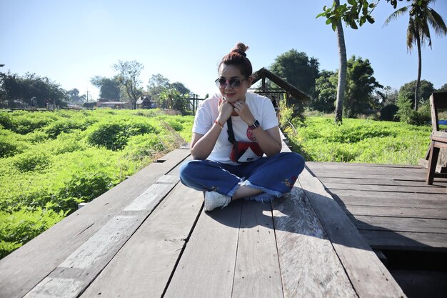 Photo portrait of woman in sunglasses sitting on boardwalk during sunny day