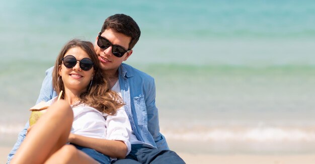 Portrait of woman in sunglasses sitting with male partner at beach