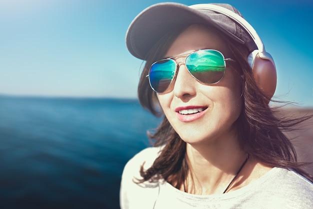 portrait of a woman in sunglasses wearing a cap who enjoys music on the background of the sea